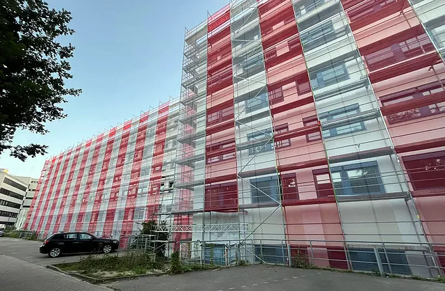 Langgezogenes Fabrikgebäude der Marzipanfabrik in Hamburg mit mehrstöckigem Fassadengerüst und rot-weißen Schutznetzen von VVV Gerüstbau.