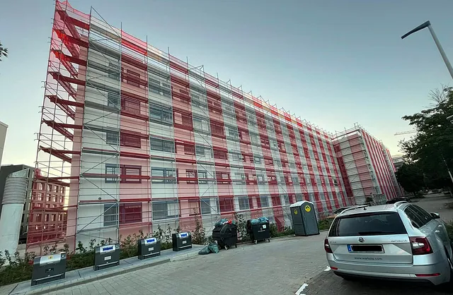 Seitenansicht der Marzipanfabrik in Hamburg mit großflächigem Fassadengerüst und rot-weißer Schutznetzverkleidung für sichere Fassadenarbeiten.