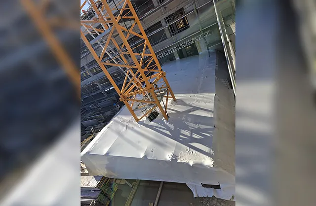 Blick von oben auf eine weiße Schutzeinhausung mit integriertem Baukranmast im Innenhof einer Baustelle in Hamburg-Barmbek.