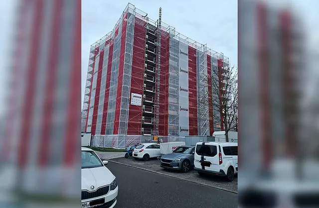 Vollständig eingerüstetes Hochhaus mit rot-weißen Gerüstschutznetzen für Fassadenarbeiten durch VVV Gerüstbau in Hamburg-Rahlstedt.