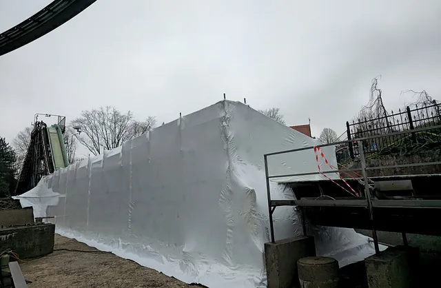 Seitliche Ansicht einer vollständig eingehausten Wasserbahn mit Gerüstkonstruktion im Heide Park Soltau für geschützte Instandhaltungsarbeiten.