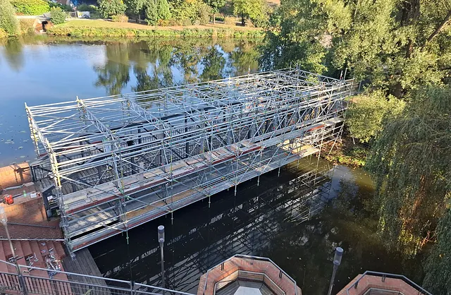 Blick von oben auf eine aufwendige Gerüstkonstruktion rund um eine Fußgängerbrücke über einem Gewässer, Spezialgerüstbau in Hamburg-Wilhelmsburg.