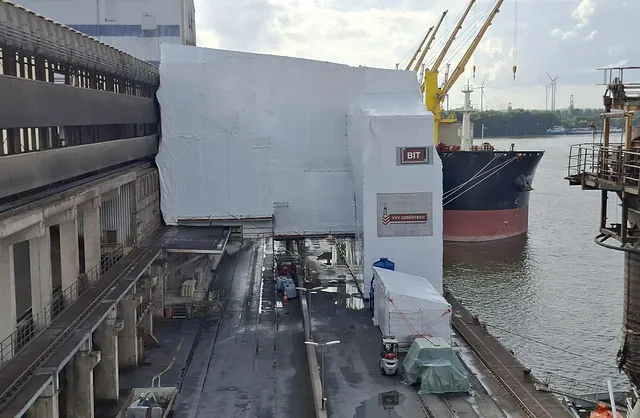 Eingehauste Industrieanlage direkt am Wasser mit Frachtschiff und Hafenkränen, Spezialgerüstbau von VVV Gerüstbau für Industrieprojekte.