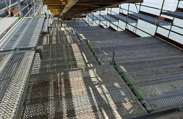 Großflächige Arbeitsplattform aus Gerüstbelägen mit Seitenschutz unter einer Stahlkonstruktion am Hafen, Spezialgerüstbau für Industrieanlagen.