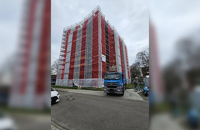 Großflächiges Fassadengerüst mit rot-weißen Schutznetzen an einem mehrgeschossigen Gebäude in Hamburg, davor ein LKW von VVV Gerüstbau.